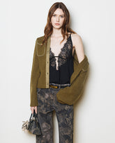 Woman with auburn hair wearing a ribbed olive green cardigan over a black top with lace inserts, paired with camouflower-print cargo trousers and a small handbag with gold details. | Pinko