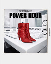 AI-generated photoshoot featuring red pointed-toe boots with ruched shafts and high heels, displayed on a white mixing console in a recording studio. Above them is the text “THE RED PLAYLIST – POWER HOUR”. | Pinko